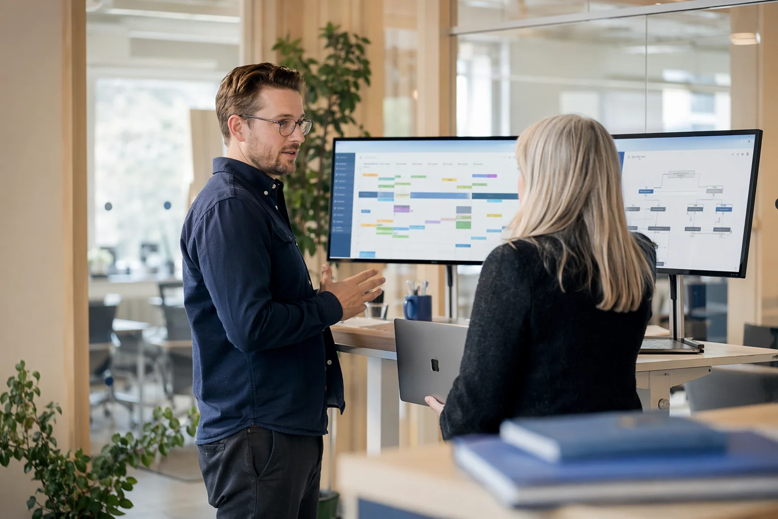 Two colleagues at a municipal IT department discussing system integrations in front of screens with timetable views.